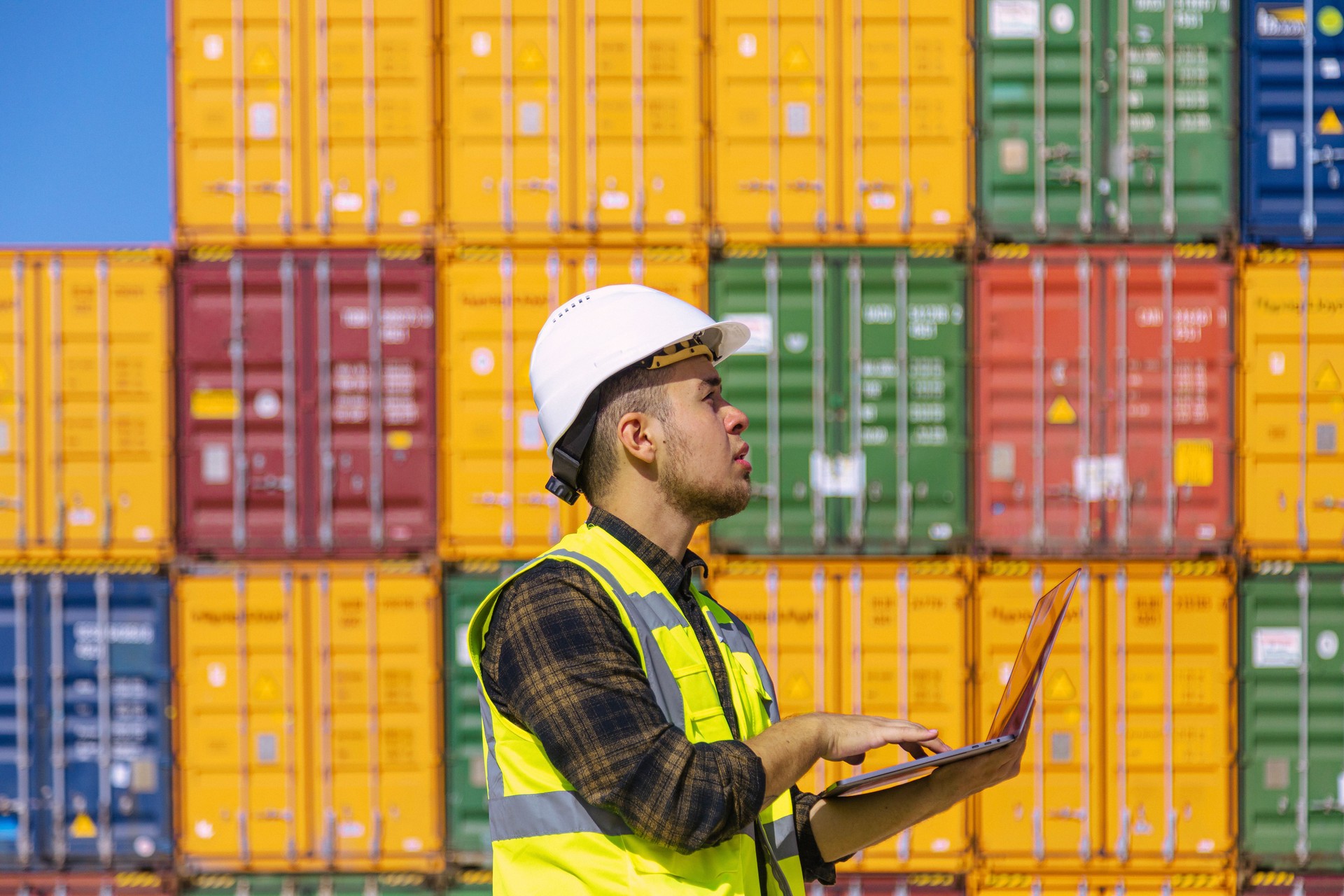 Portrait of logistic engineer man standing and working with laptop computer outside on a large commercial dock